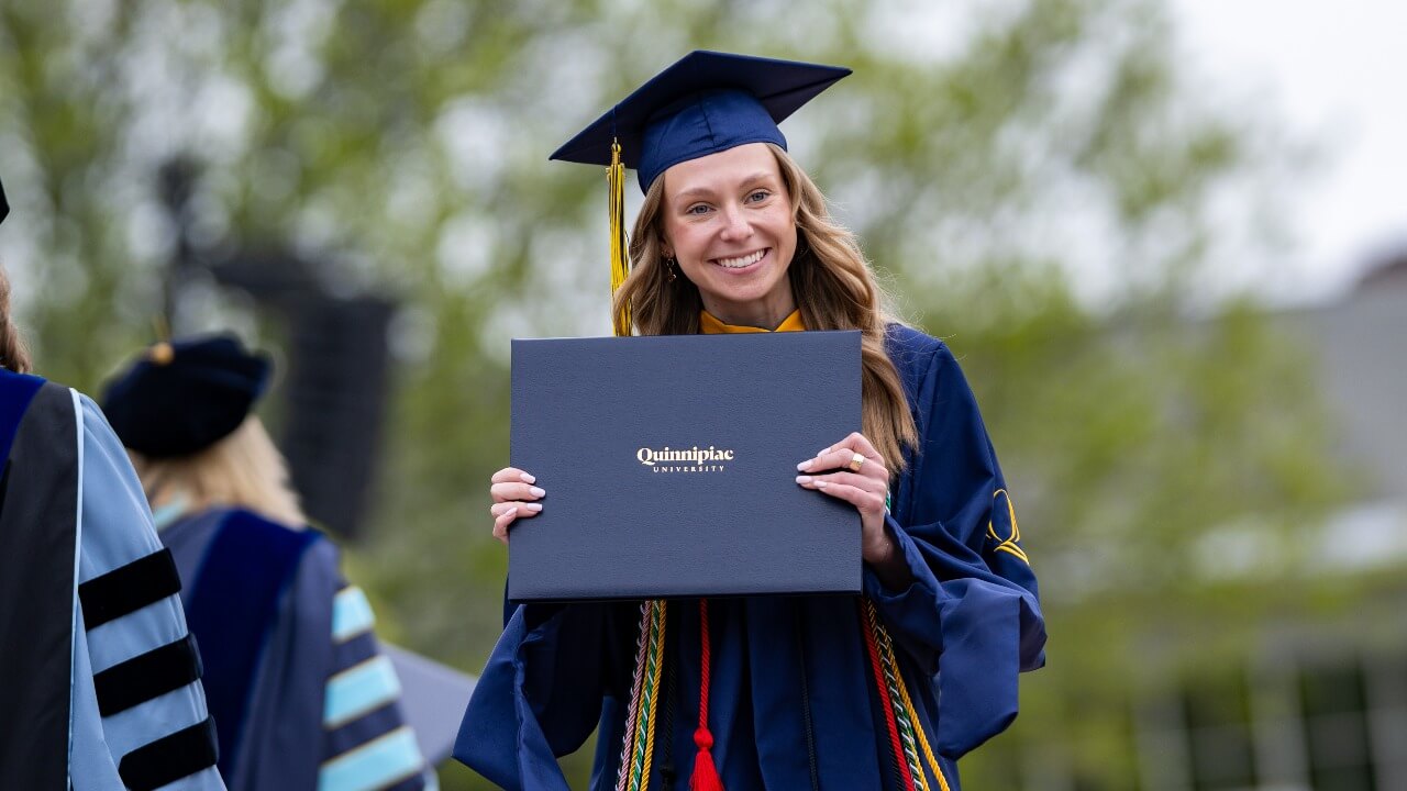 graduate holding diploma and smiling for a photo