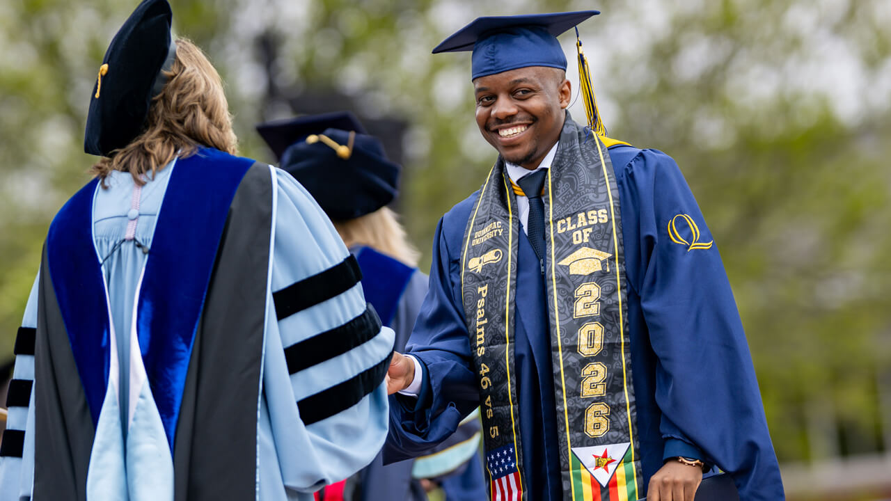 A graduate in a Class of 2026 stole and gown shakes hands with a dean