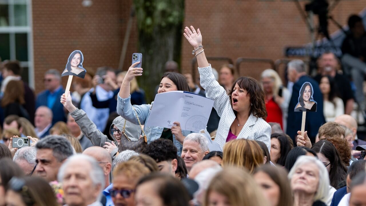family stands up hollering with excitement and holding up signs of their graduates face