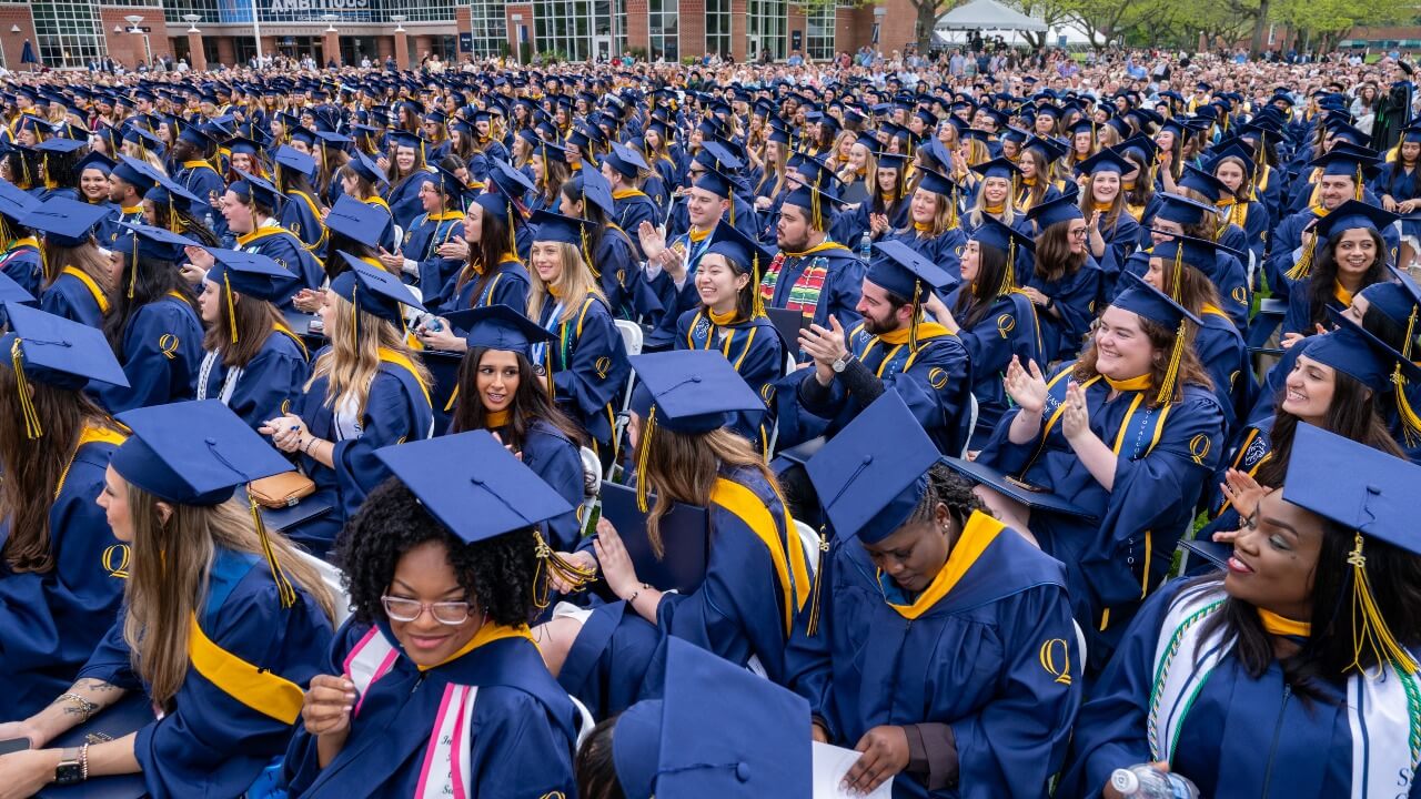 Graduates in caps and gowns stand in a crowd.