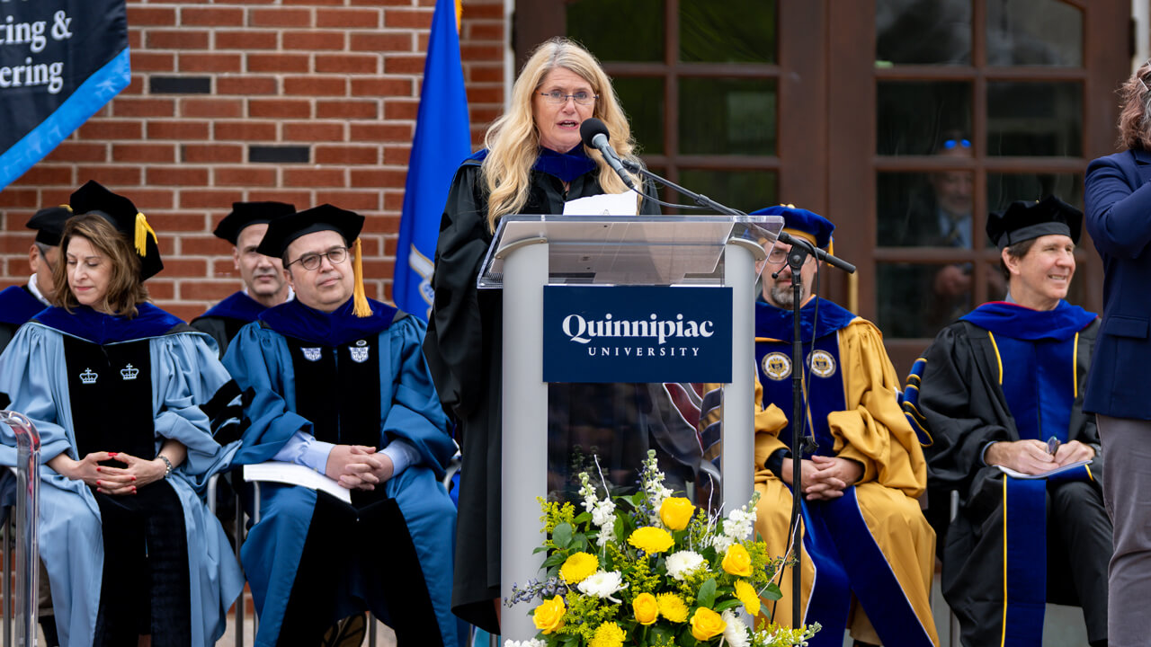 Pam Martinez speaks at the podium on the library steps with staff seated behind her