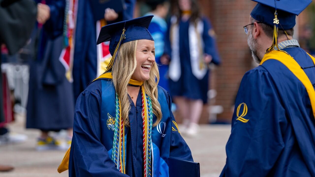 Graduate in cap and gown smiles at faculty member
