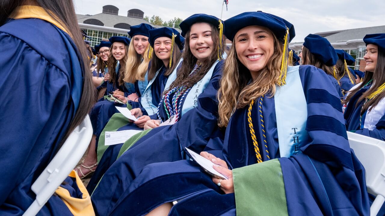 Row of graduates in caps and gowns smile for a photo.