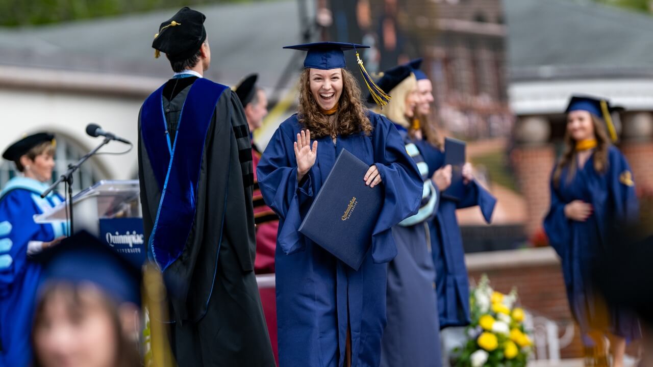 Graduate in cap and gown shakes hand with Dean on stage.