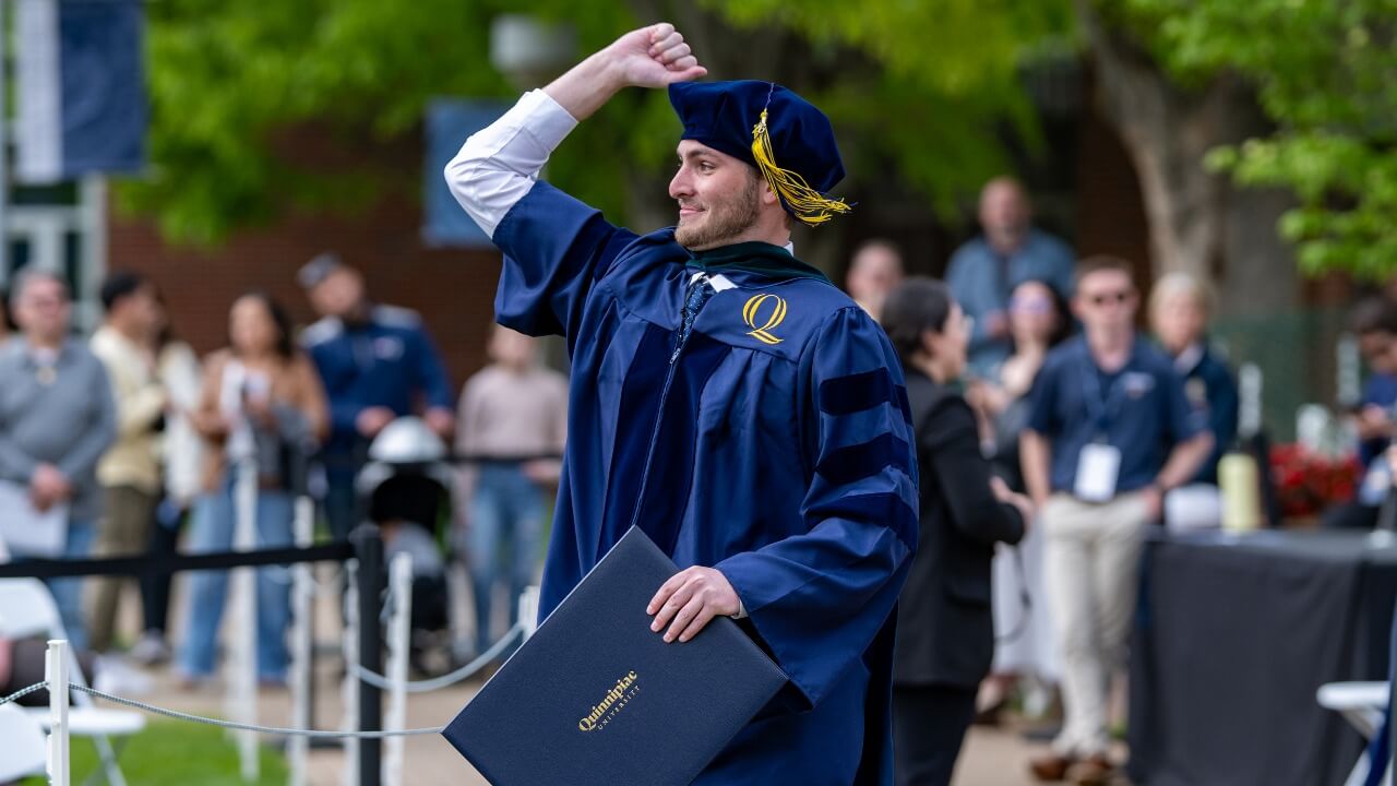 excited graduate fist bumping to the sky and holding his diploma