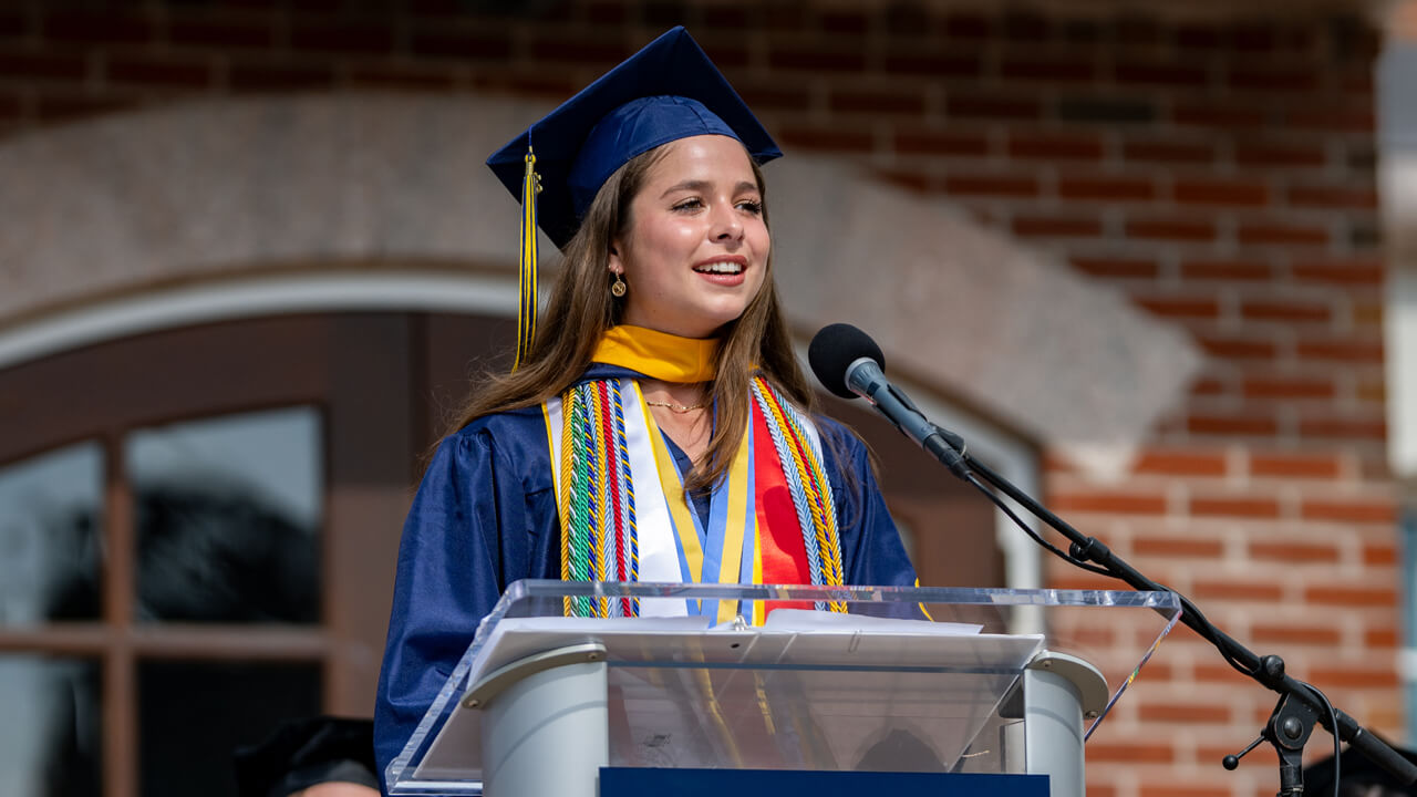 Sophia Konkolics speaks at the Quinnipiac podium in her Commencement robe