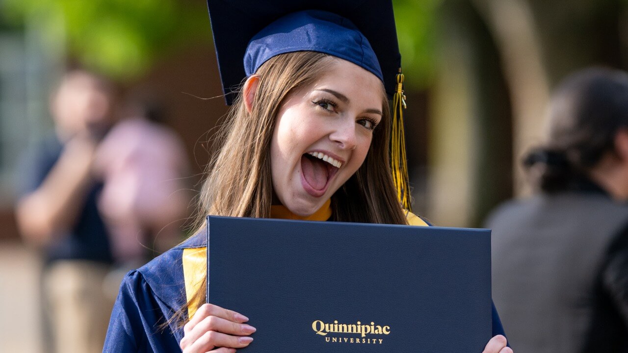 Graduate smiles in excitement holding their degree.