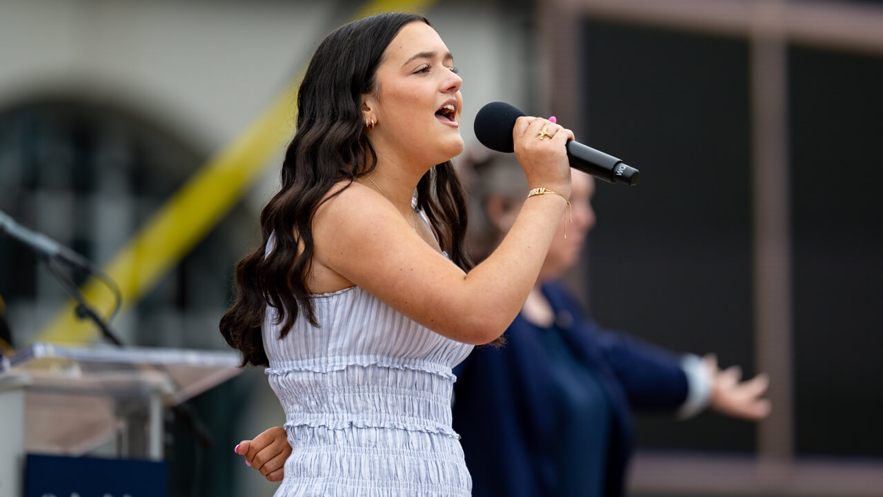 Addison Prunier holds a microphone and sings on the library steps