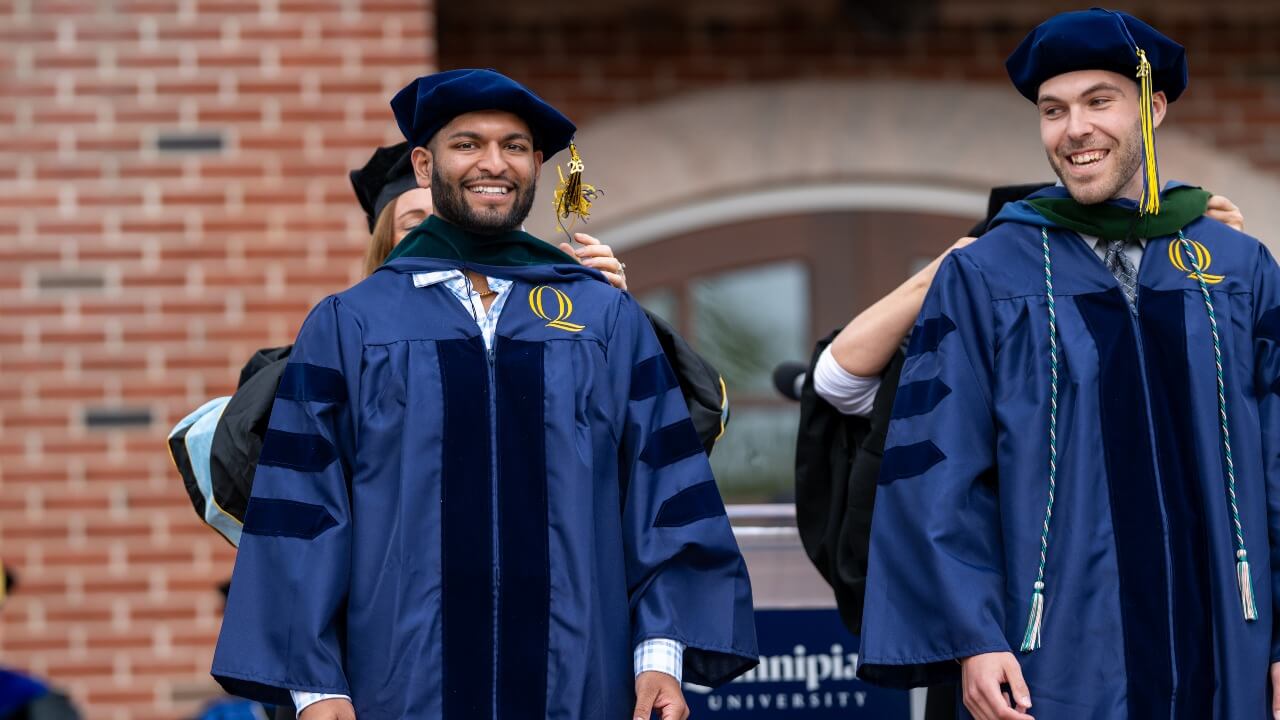 Two graduates in caps and gowns receive their hoods.