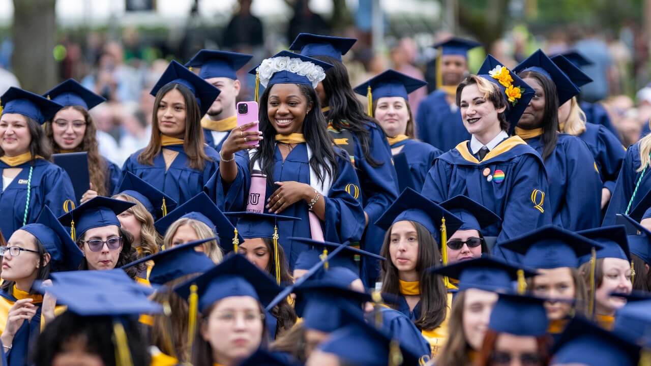 hundreds of graduates in their cap and gowns watching the ceremony