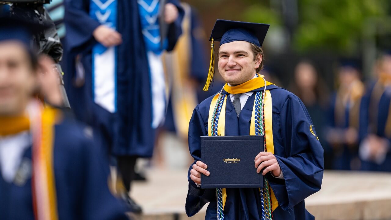 Class of 2026 Student Government President smiling while holding up his diploma