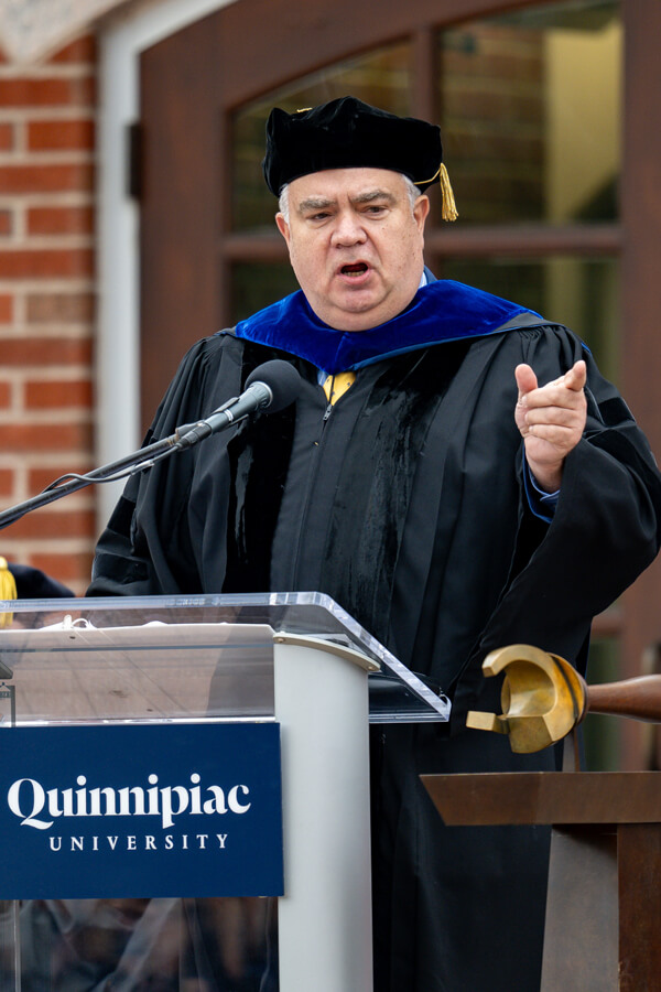 Robin Hayes speaks from a podium on the library steps with Commencement mace in the foreground