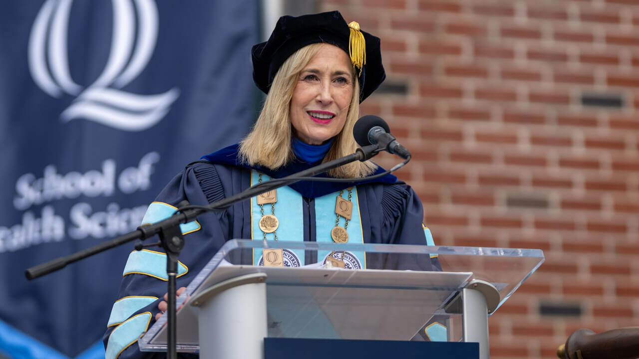 Marie Hardin in her blue Commencement robes speaks at the podium