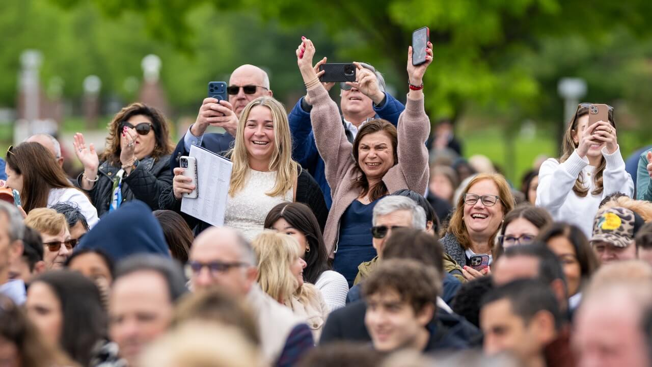 Family and friends of graduates stand and cheer while in the audience