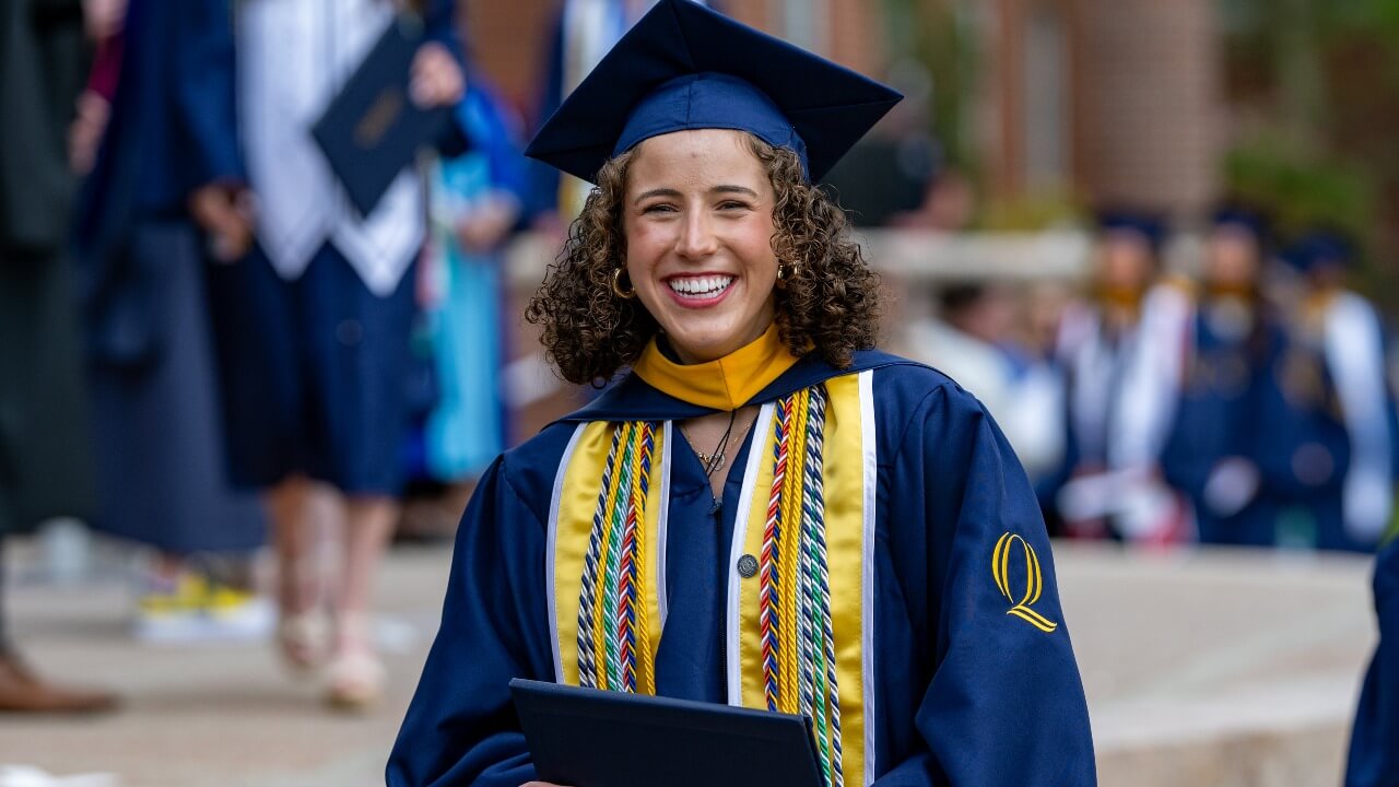 a graduate laughing with joy, holding their diploma smiling to the camera