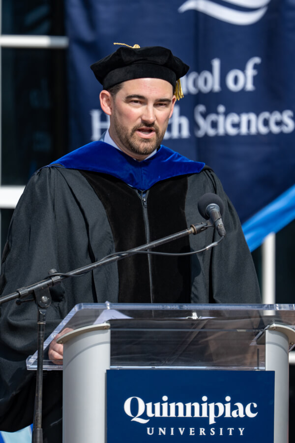 Mike Papale speaks at the podium with the health sciences flag behind him