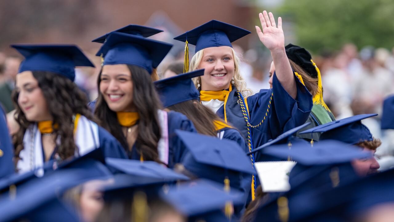 Graduate in cap and gown waves to the camera in the crowd.
