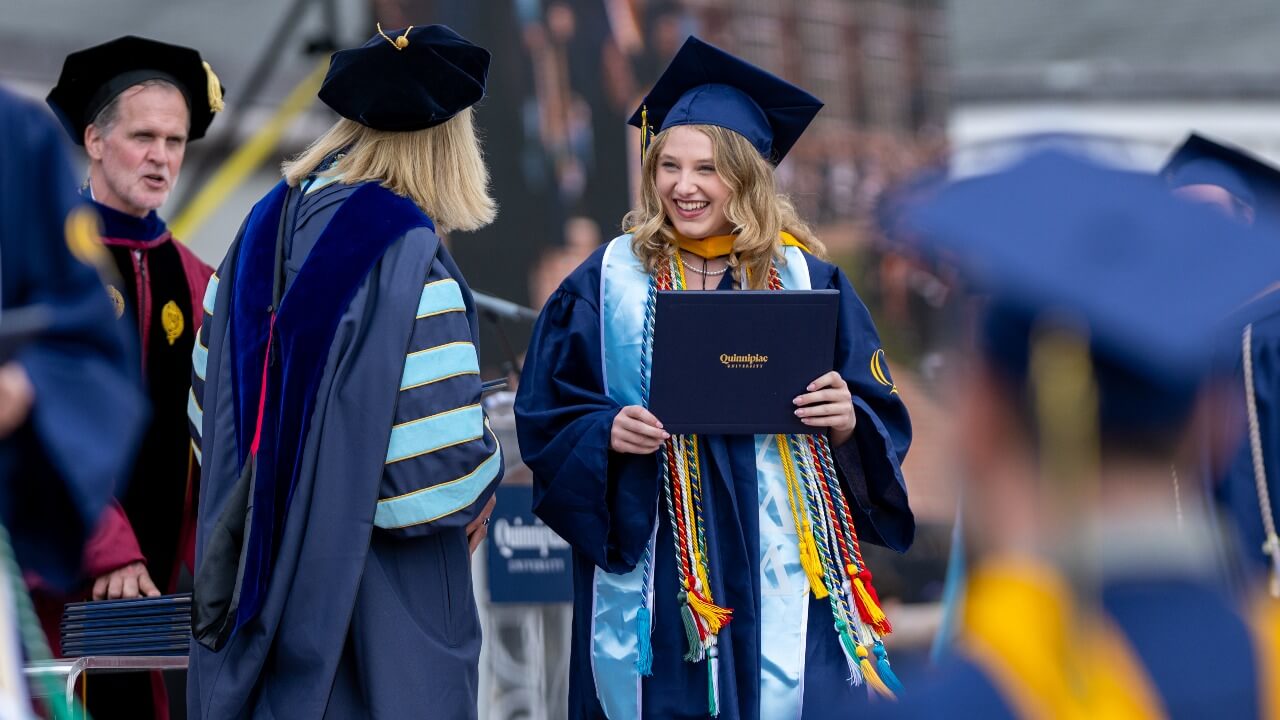 Graduate in cap and gown smiles at Marie Hardin while on stage.