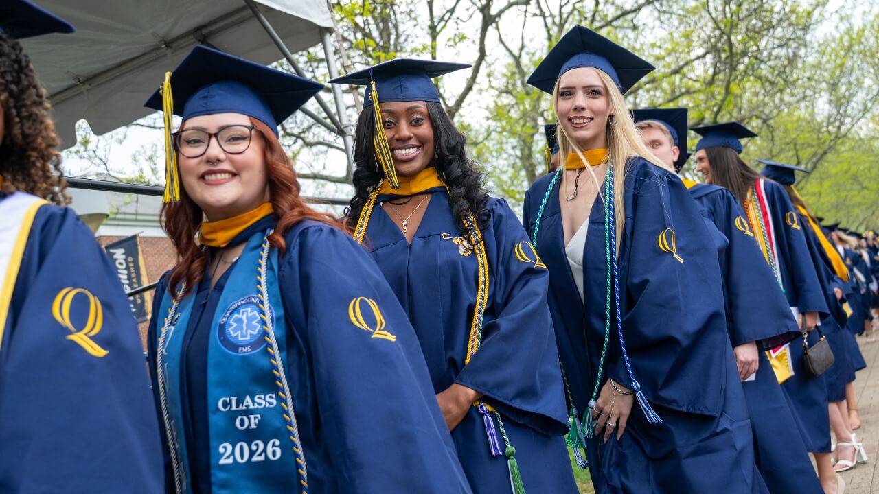 a sea of graduates walking in line while two smile right at the camera