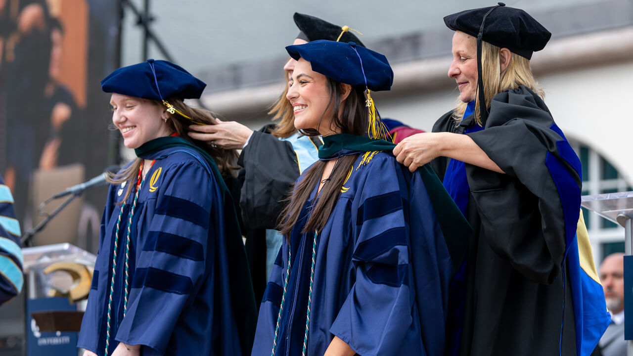 Two graduates receive their hoods from faculty members on stage