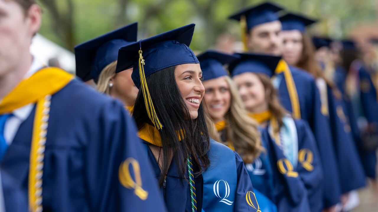 Graduates lining up before walking across the stage, one graduate looking out to the right