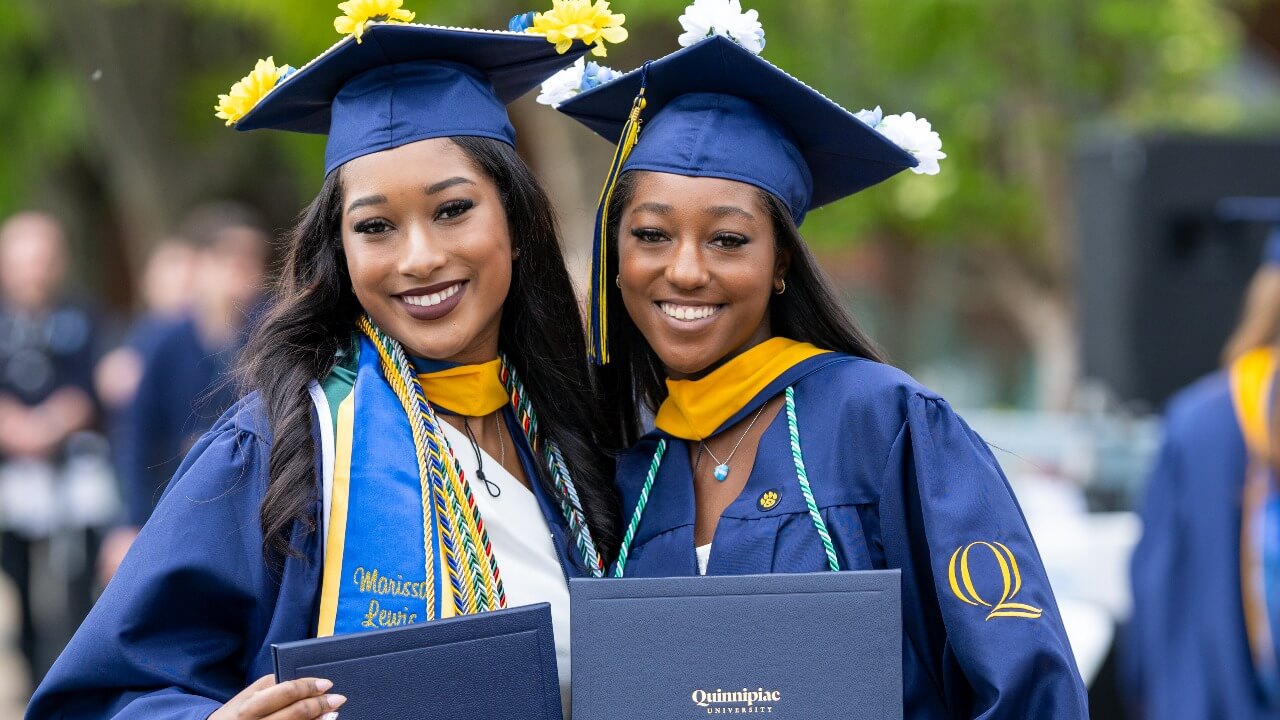Two sisters smiling together with their newly earned diplomas