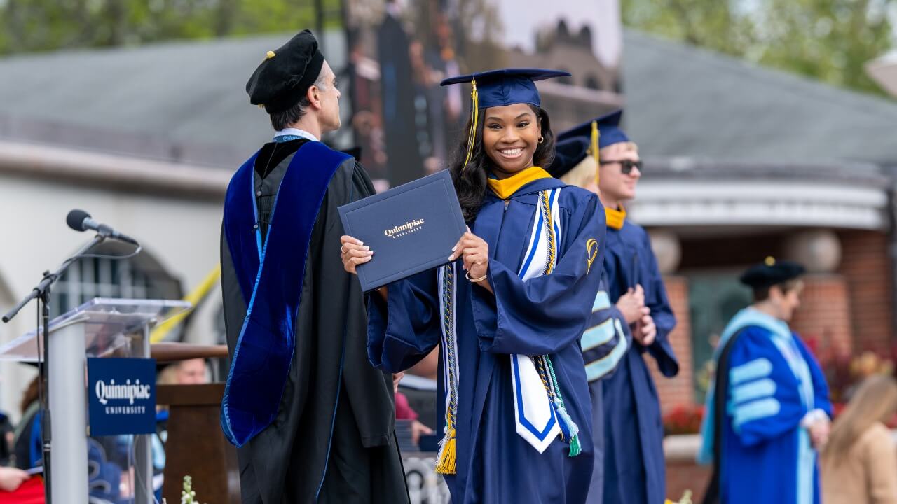 Graduate holding up a diploma next to her while she walks off the library steps