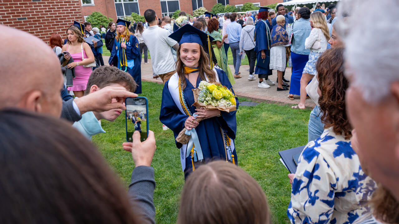 A graduate holds yellow flowers and poses for a photo for her loved one