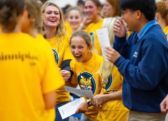 A new student in a gold Bobcats shirt doubles over with laughter surrounded by new students