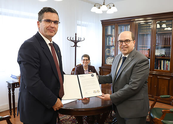 Óbuda University Rector Levente Kovács shaking hands with Dean of the School of Computing & Engineering Taskin Kocak. Provost Debra Liebowitz sitting at the agreement table.