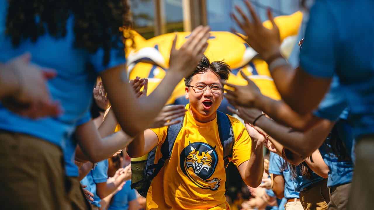 A student in gold Bobcat shirt cheers and runs through a line of people giving high fives