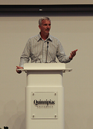 Jason Burke standing at the Quinnipiac podium