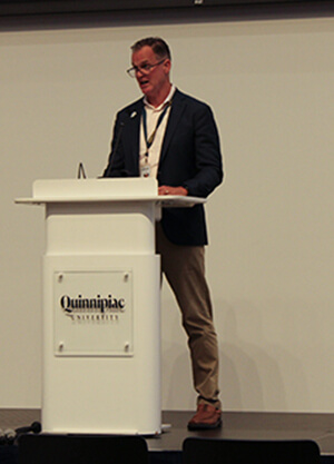 Tom Ellett standing at the Quinnipiac podium