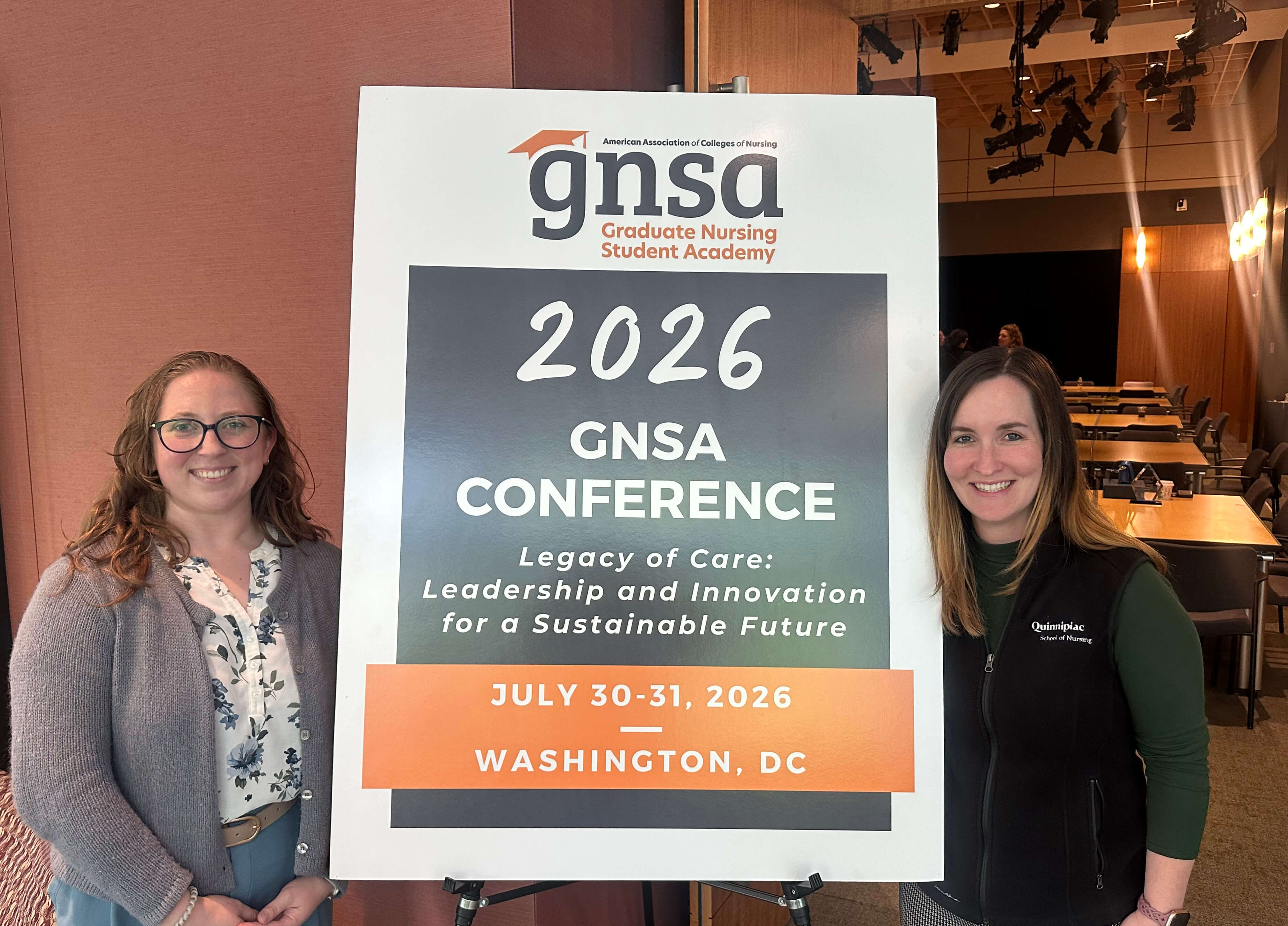 Two School of Nursing students pose together with a sign at a conference