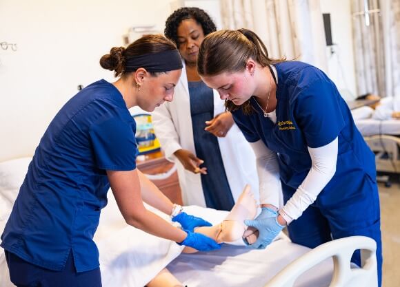 Two nursing students wrapping a mannequin's foot