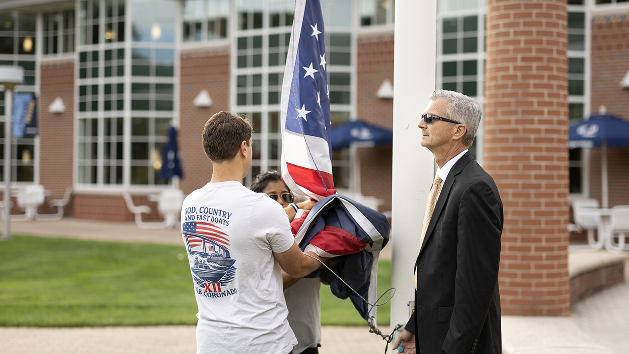 Two students helping Jason Burke raise the flag to half mast